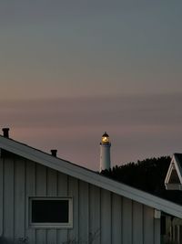 Lighthouse by illuminated building against sky at sunset