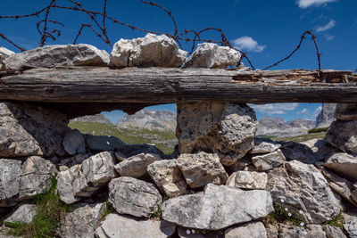 Stone wall by rocks against blue sky