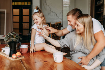 A happy family with a child having breakfast drinking tea laughing and having fun at home