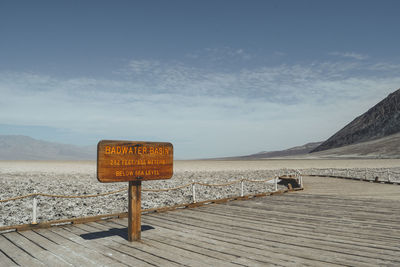 Information sign by sea against sky