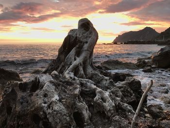 Rock formation on shore against sky during sunset