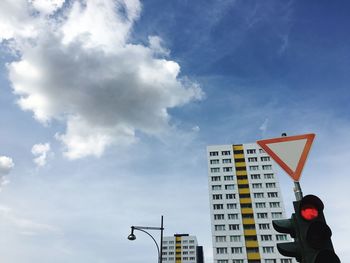 Low angle view of stoplight with road sign and buildings against sky