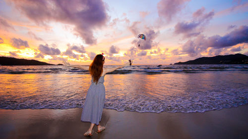 Rear view of woman standing on beach against sky during sunset