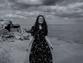 Young woman standing at beach against sky