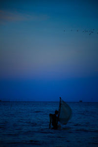 Man on boat in sea against sky during sunset