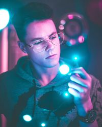 Close-up of young man wearing eyeglasses holding illuminated light