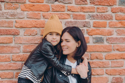 Portrait of a smiling young woman against brick wall