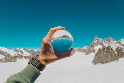 Cropped hand holding crystal ball against mountains during winter