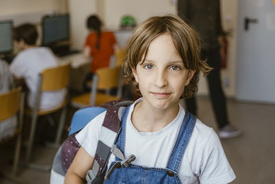 Portrait of blond girl carrying backpack in computer classroom at school