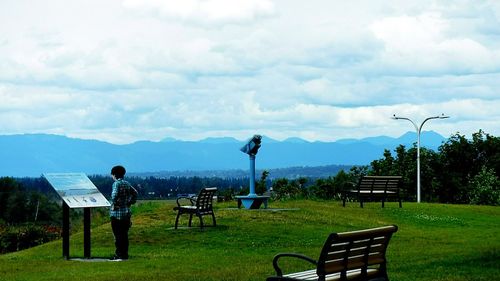 People sitting on grassy field against cloudy sky