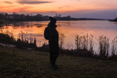 Girl in winter clothes stands on a lake at sunset