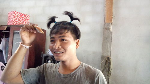 Smiling young man with pigtails standing at home