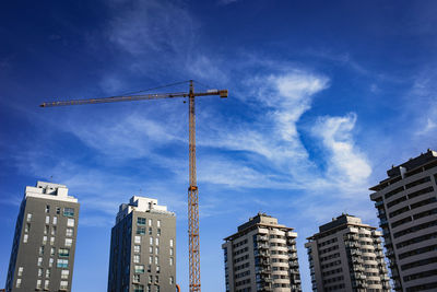 Low angle view of crane and buildings against blue sky