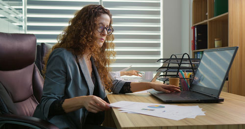 Business women comparing data from reports and laptop.