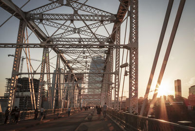 People walking on bridge against sky in city during sunset