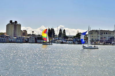 Sailboats in sea by buildings against clear sky