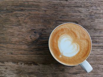 Heart-shaped latte coffee on wood floor.