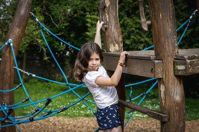 A girl climbs a rope swing on a tree in the park.