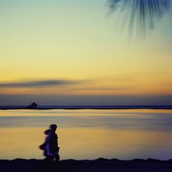 Silhouette woman standing by sea against sky during sunset