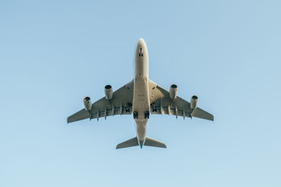 Low angle view of airplane flying against clear blue sky