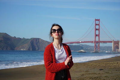 Young man wearing sunglasses standing on bridge over sea against sky
