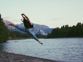 Woman jumping at lakeshore against sky