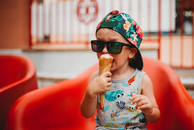 Young toddler eating ice cream cone with cap to back and sunglasses