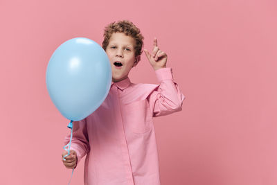 Boy holding balloon standing against pink background
