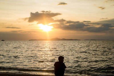 Silhouette person on sea against sky during sunset