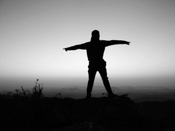 Silhouette man with arms outstretched standing on mountain against sky