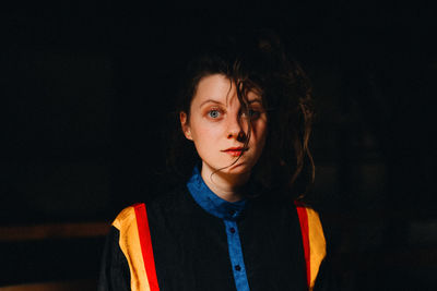 Portrait of young woman standing against black background