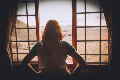 Rear view of woman looking through window at home