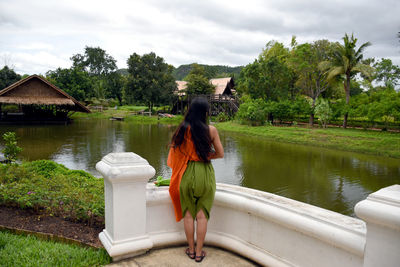 Rear view of woman standing by lake against sky