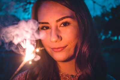 Portrait of beautiful young woman standing against trees in park at night