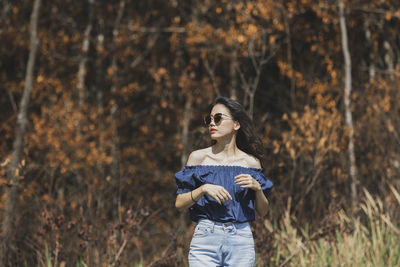 Woman wearing sunglasses standing on field against forest