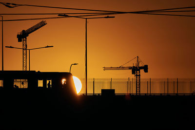 Silhouette cranes at construction site against sky during sunset