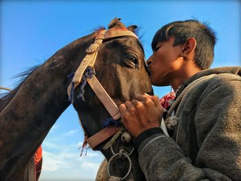 Low angle view of man kissing horse against sky