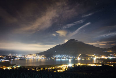 Illuminated cityscape by mountains against sky at night