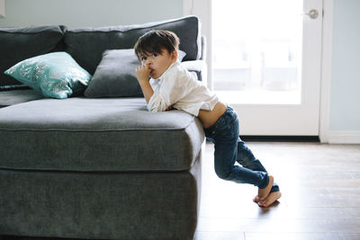 Boy looking away while leaning on sofa at home