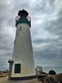 Lighthouse on beach against cloudy sky