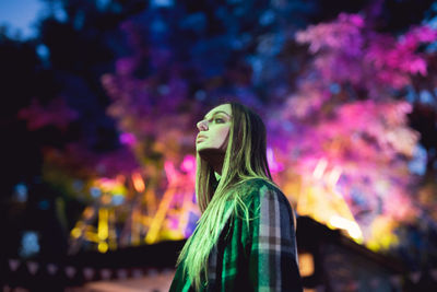 Portrait of woman standing against illuminated christmas tree