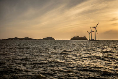 Traditional windmill by sea against sky during sunset