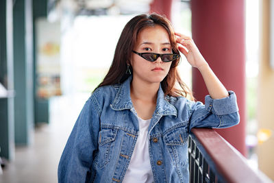 Portrait of beautiful young woman wearing sunglasses standing by railing