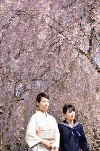 Women in kimono standing against cherry tree