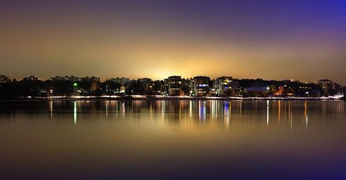 Illuminated buildings by river against sky at night