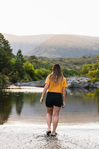 Full length rear view of woman standing by lake