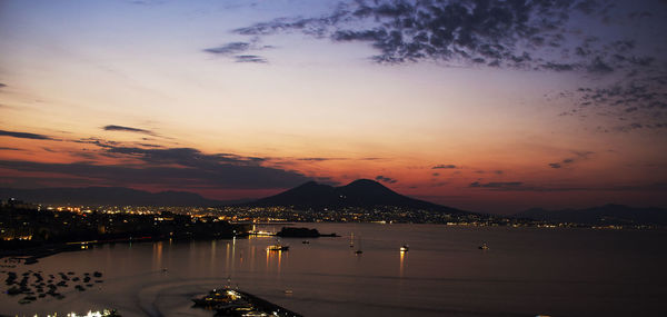 Illuminated city by sea against sky during sunset