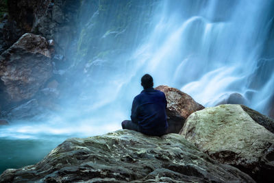 Rear view of man looking at sea against rock formation