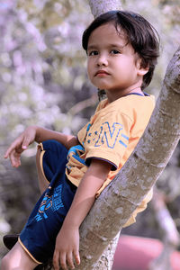 Cute boy looking away while sitting on tree