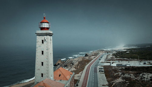 Lighthouse amidst buildings and sea against sky